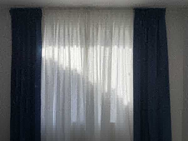 Custom pinch-pleat navy drapery panels with white sheer curtains